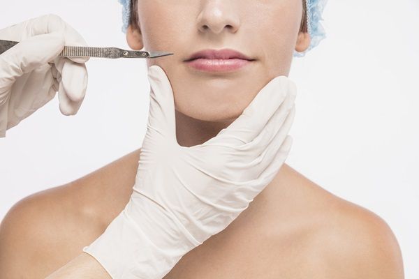 Médico de clínica estética sostiene en su mano un bisturí frente al rostro de una mujer joven