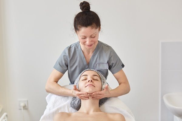 Masajista realizando un masaje relajante en el rostro de una mujer joven