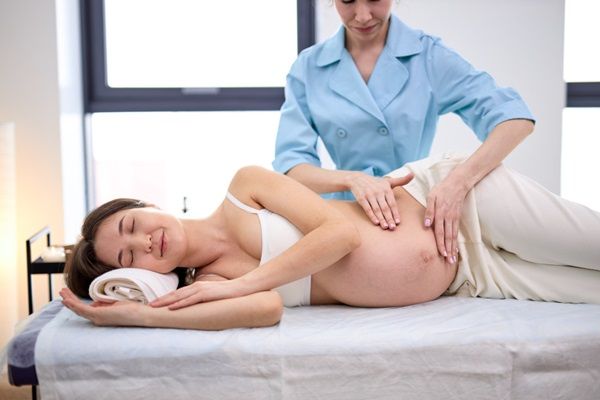 Masajista aplicando un aceite para masajes en la barriga de una mujer embarazada