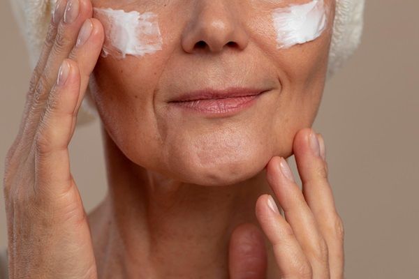 Mujer mayor colocándose crema hidratante en la cara