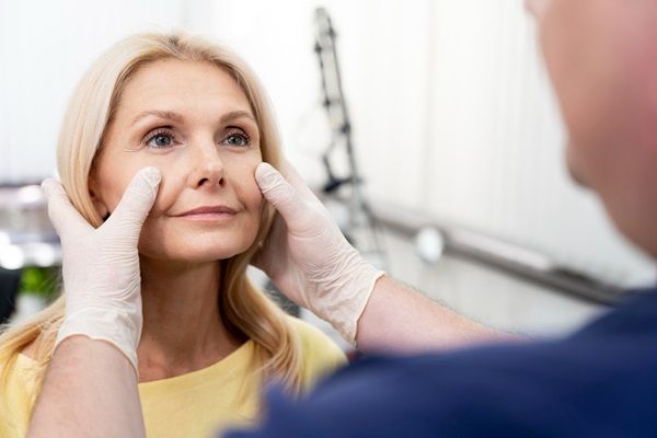 Blefaroplastia - Médico estético estirando la piel del párpado inferior de una mujer para evaluar si es apta para la blefaroplastia