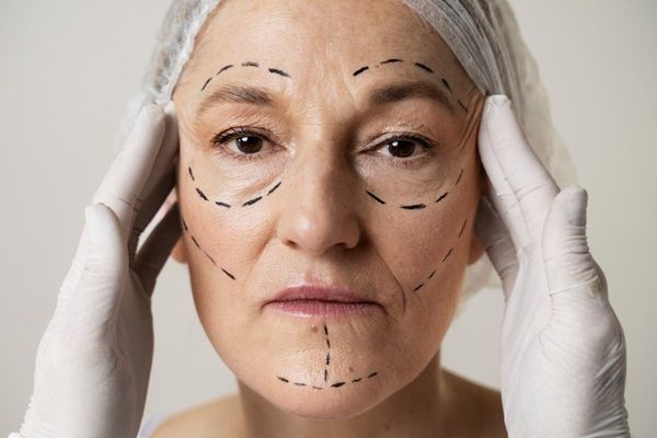 Médico estético tocando la cara de una mujer que tiene en su rostro el boceto del tratamiento de rejuvenecimiento facial