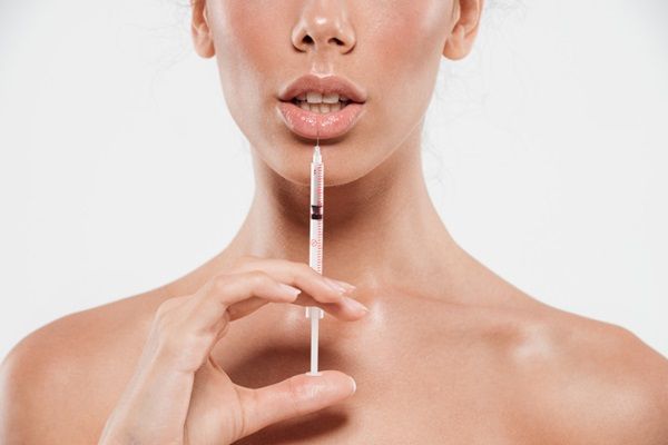 Mujer sosteniendo una inyectadora cerca de su boca como referencia a un tratamiento de aumento de labios