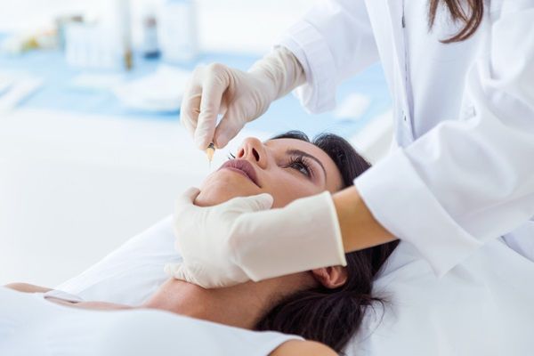 Bótox o ácido hialurónico - Esteticista aplicando una inyección de ácido hialurónico Madrid en los labios de una mujer joven