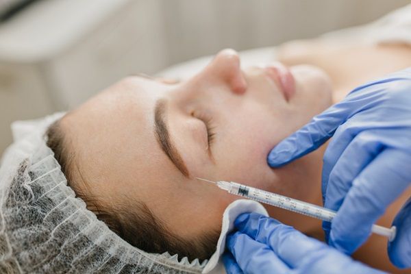 Bótox o ácido hialurónico - Médico utilizando la estructura bótox para crear un contorno facial más suave en el rostro de una mujer