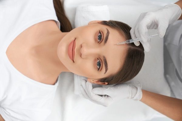 Especialista estético aplicando un tratamiento de rejuvenecimiento facial a una paciente femenina