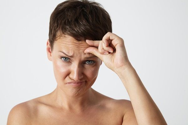 Cómo hidratar la piel - Mujer con cara de tristeza tocándose las arrugas de la frente por no utilizar cremas hidratantes