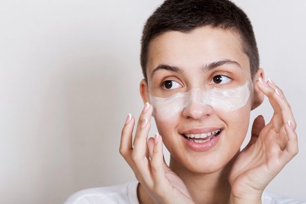 Mujer de cabello corto aplicándose una de las mejores cremas hidratantes en la cara