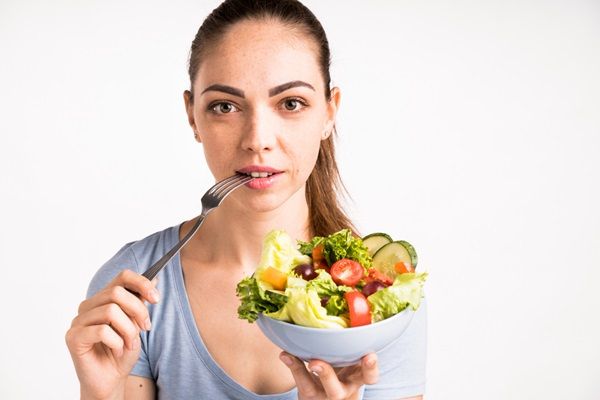 Mujer sosteniendo un plato de ensalada con un tenedor en la boca para comer saludable y cuidar la piel