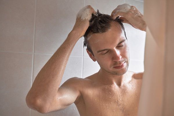 Hombre haciéndose un masaje en el cuero cabelludo mientras lava su cabello para estimular el crecimiento del pelo luego de un injerto capilar
