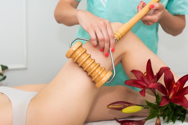 Maderoterapia - Esteticista realizando un tratamiento de maderoterapia corporal en las piernas de una mujer