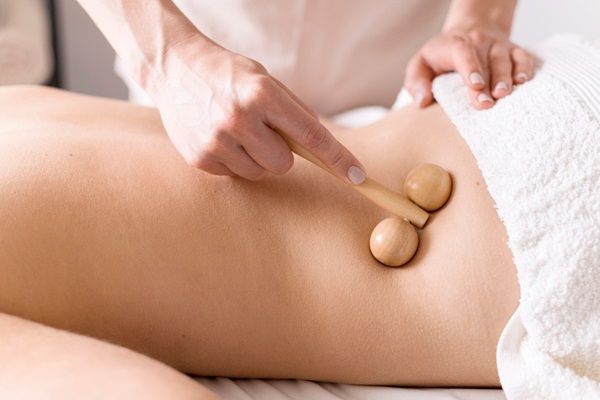 Maderoterapia - Esteticista profesional utilizando una herramienta de madera para realizar masajes corporales en la espalda baja