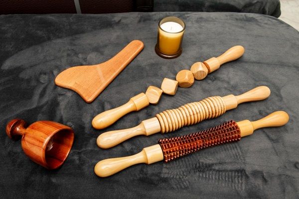 Diversas herramientas de madera como rodillos, copas y espátulas sobre una cama para masajes