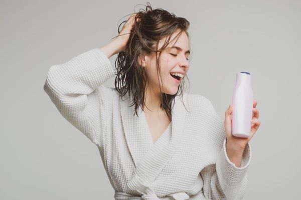 Regeneradores de cabello - Mujer feliz tocándose el pelo luego de usar un champú regenerador para reparar el cabello