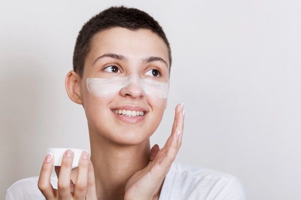 Mujer sonriente aplicándose crema humectante en el rostro para nutrir e hidratar la piel