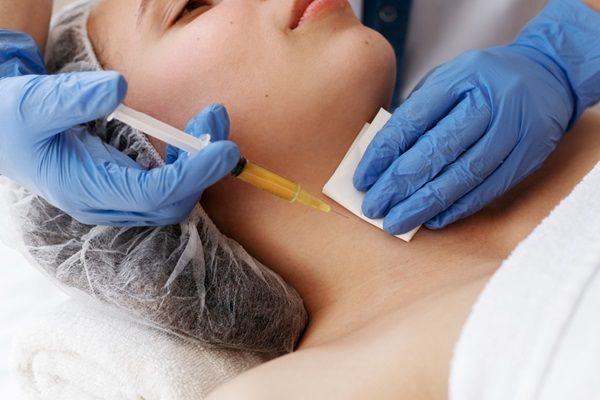 Médico estético aplicando una inyección de ácido hialurónico Madrid para hidratar la piel del cuello de una mujer y eliminar las arrugas dinámicas