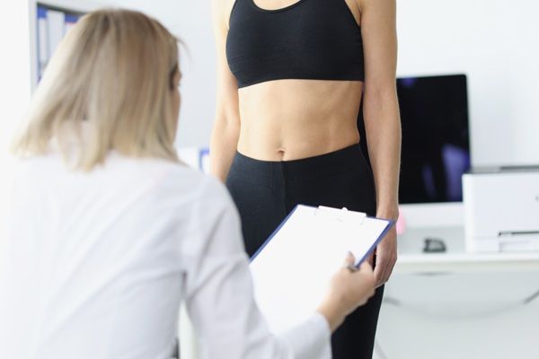Reducir la grasa - Médico estético evaluando a una mujer con grasa localizada para diseñar un tratamiento que ayude a reducir la grasa abdominal