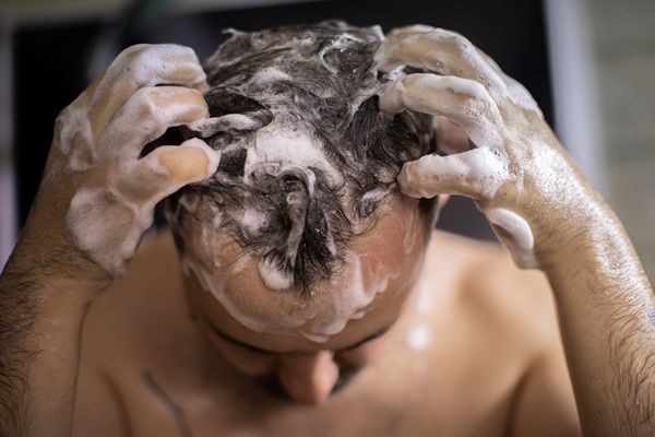 Hombre lavando su cabello con abundante champú para limpiar el cuero cabelludo y estimular el crecimiento del pelo