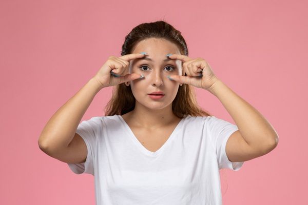 Ojeras - Mujer estirando la piel de su rostro para disimular las ojeras y arrugas del entrecejo antes de realizarse tratamientos estéticos en las clínicas estéticas mejor valoradas Madrid