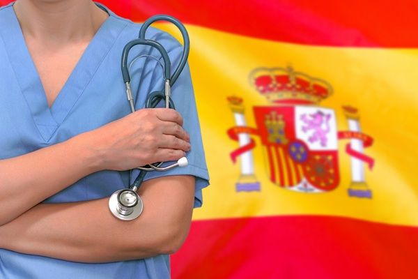 Turismo médico España - Médico de la mejor clínica injerto capilar España sosteniendo un estetoscopio frente a una bandera de España